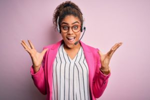 Young african american call center agent girl wearing glasses working using headset celebrating crazy and amazed for success with arms raised and open eyes screaming excited because she works in a customer-centric call center